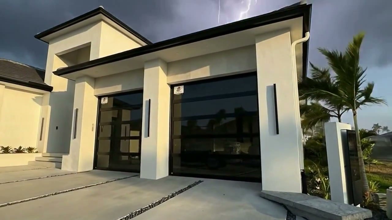 A modern South Florida luxury home with full-view impact glass AA Impact garage doors standing strong as a thunderstorm rolls in