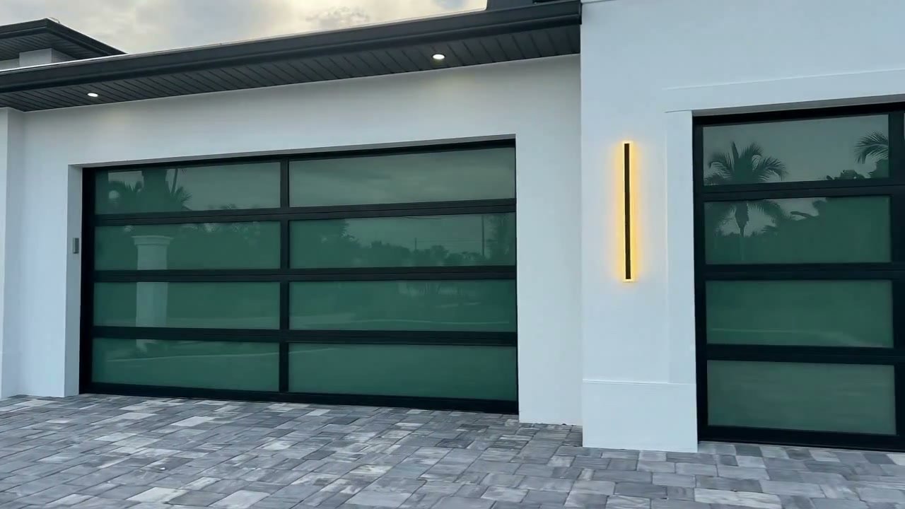 Full-view impact glass AA Impact garage doors installed on a modern white South Florida home at dusk