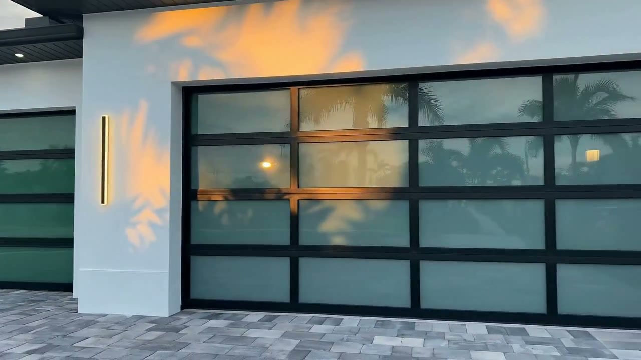 AA Impact Series 1800 flagship full-view impact glass garage door on a luxury South Florida home, warm sunset reflected in the glass