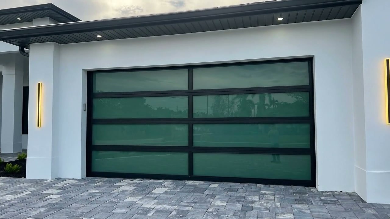 Head-on view of a black-frame full-view impact glass AA Impact garage door on a modern white South Florida home at twilight