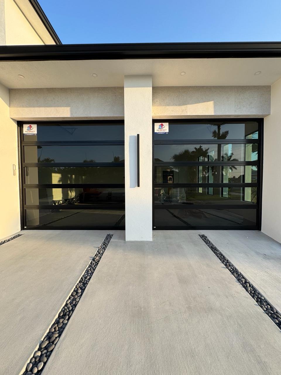 Twin black full-view impact glass garage doors split by a white column on a South Florida home