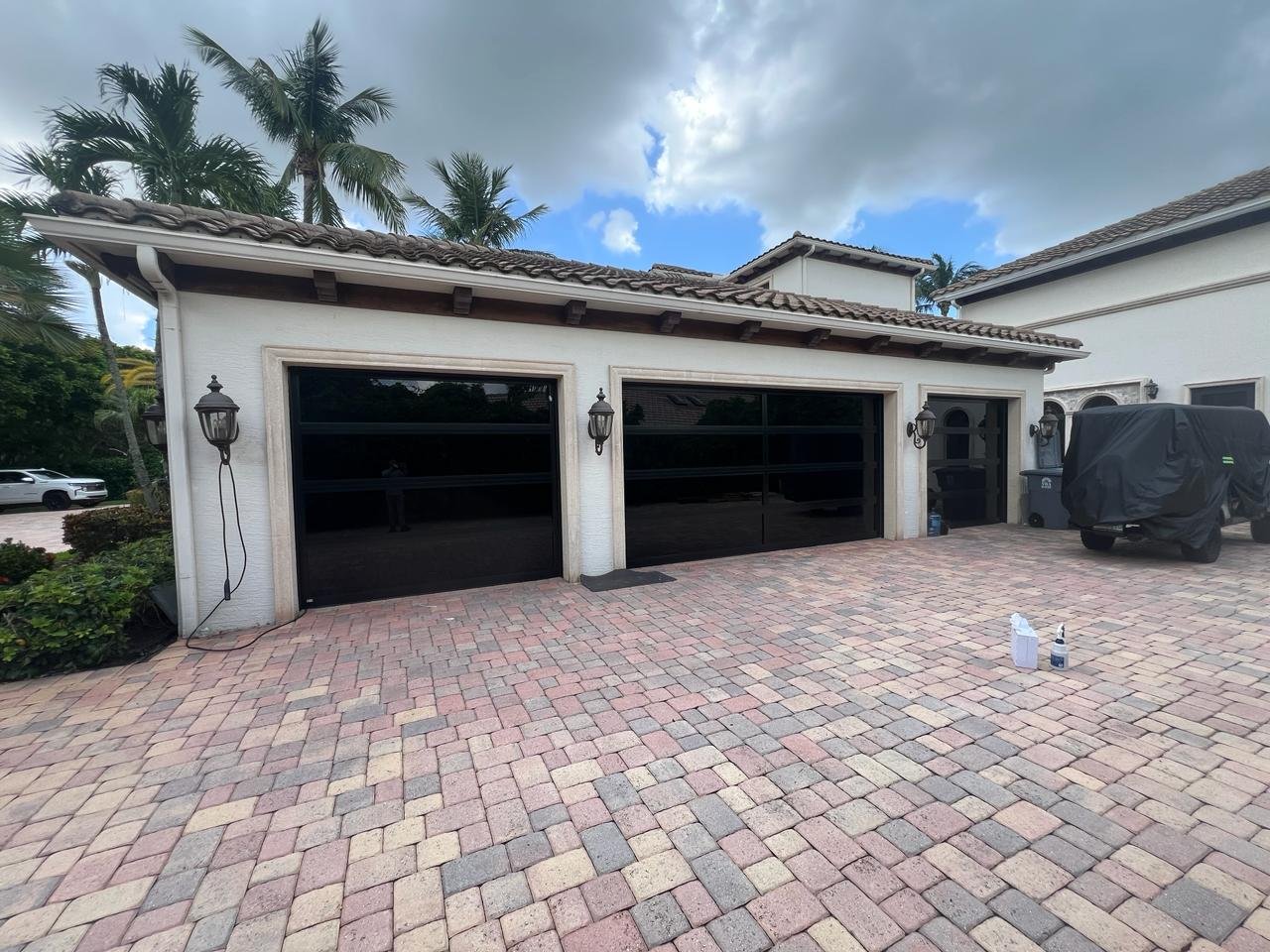 Three black full-view impact glass garage doors on a Mediterranean-style South Florida home framed by palms