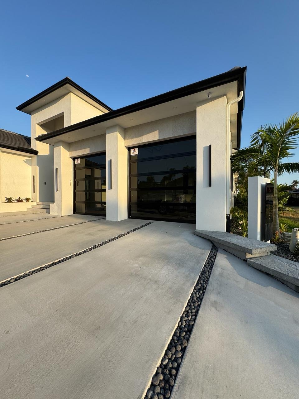 Modern flat-roof South Florida home with two dark full-view impact glass garage doors at golden hour