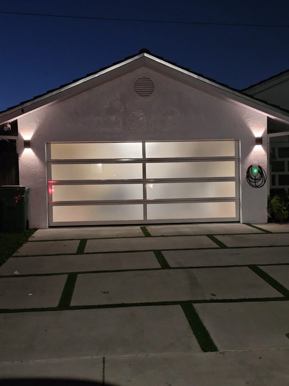 Frosted white full-view impact glass garage door glowing warm at night on a South Florida home